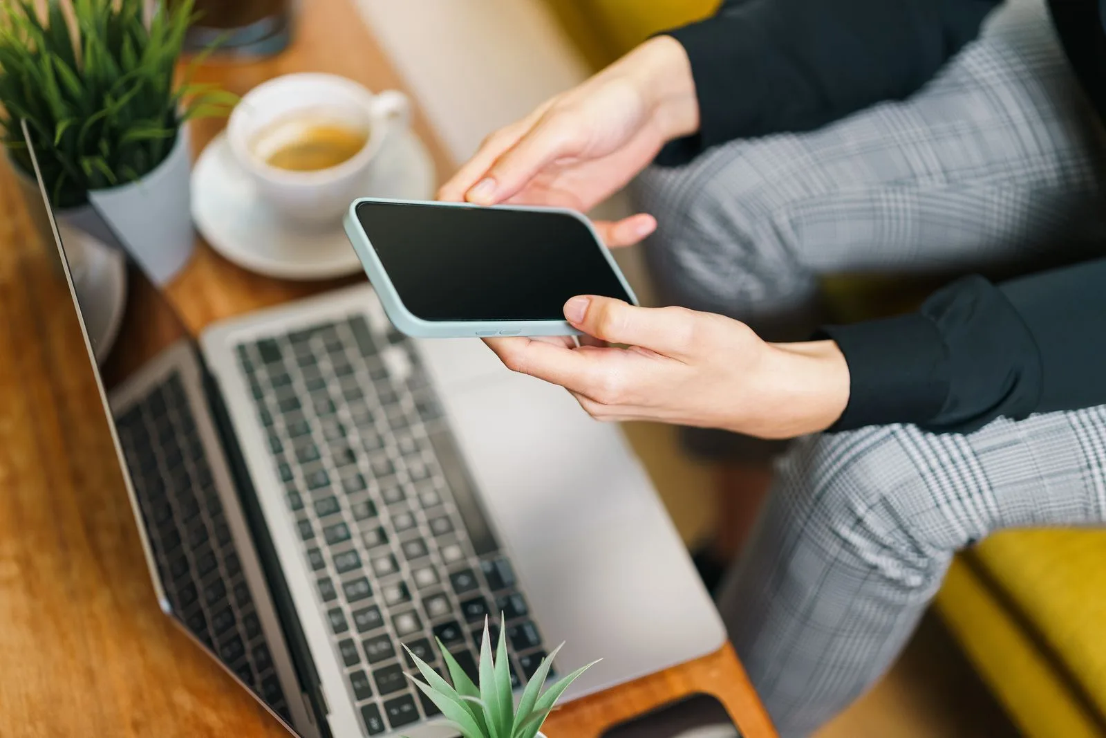 Close-up of hands checking a Meta ad account setup on a smartphone next to a laptop